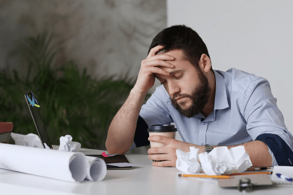 Tired business owner at a desk with paperwork and a laptop